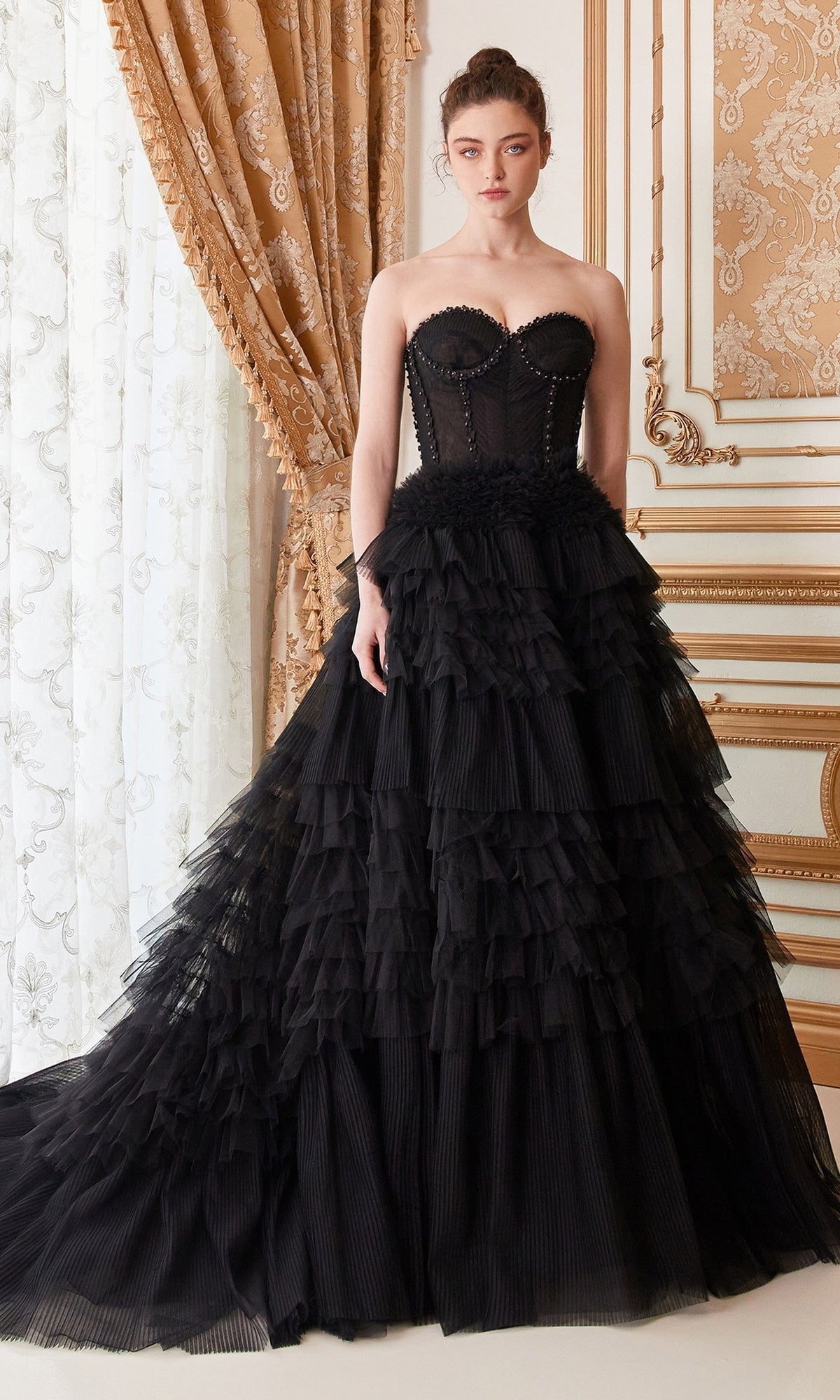 A woman wearing the Strapless Tiered Long Prom Ball Gown A1017, featuring a fitted bodice and layered tulle skirt, stands in an ornate room with gold detailing and patterned curtains.